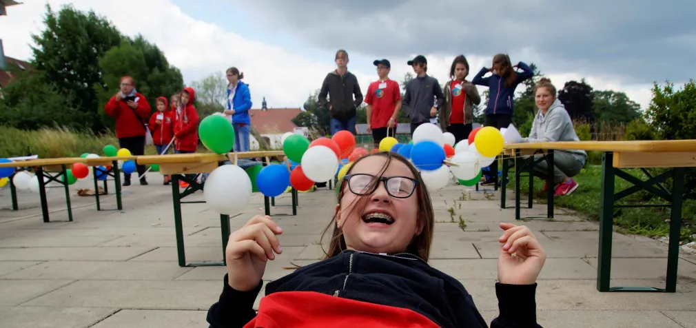 Ein Kind lacht in die Kamera und im Hintergrund sind Luftballons zu sehen