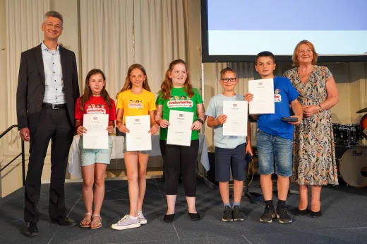 Das Bild zeigt die fünf ausgezeichneten Juniorhelfer:innen sowie Staatsminister Piazolo und Ehrenamtsbeauftragte Eva Gottstein, die geminsam für ein Gruppenfoto posieren.