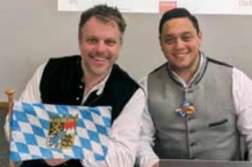 Jörg und Kirk sitzen in Tracht nebeneinander vor einer Bayernfahne Jörg und Kirk sitzen in Tracht nebeneinander vor einer Bayernfahne