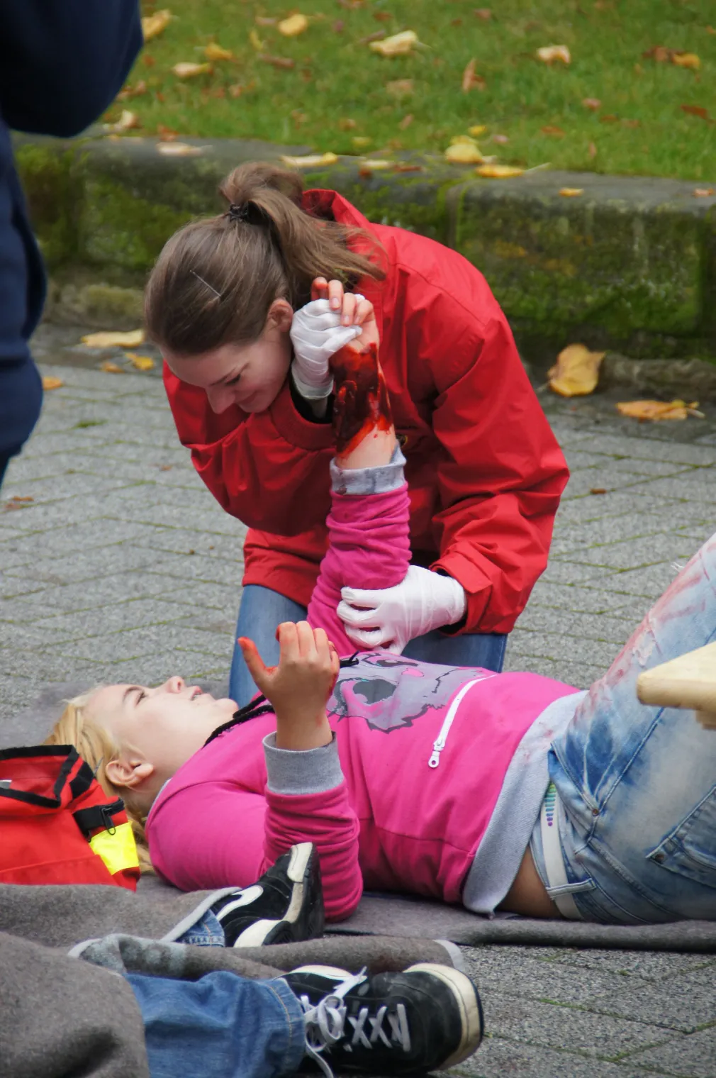 Ein JRK-Mitglied hilft einer verletzt und am Boden liegenden Person und versorgt diese