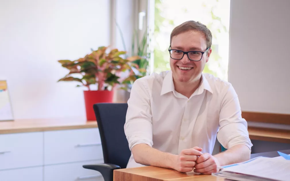 Philipp Seitz sitzt mit weißem Hemd an einem Schreibtisch