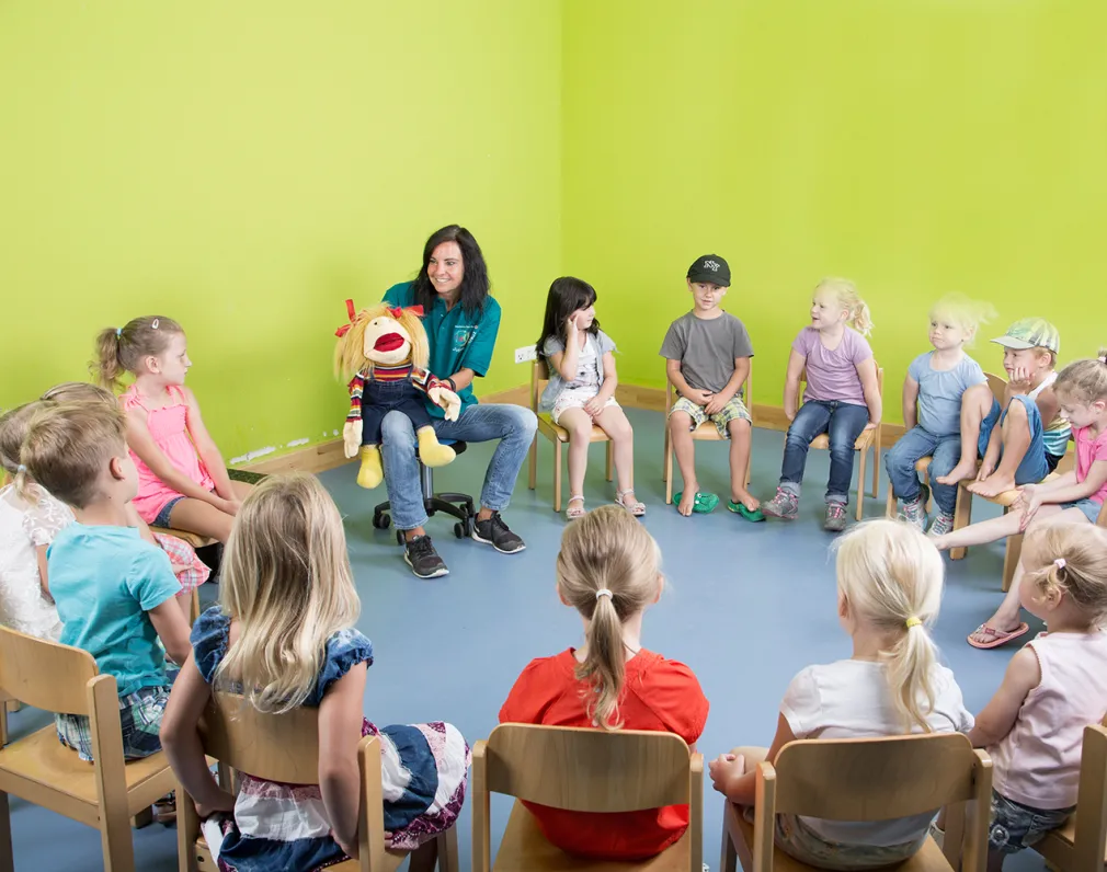 Kinder sitzen im Stuhlkreis und eine Handpuppe erzählt ihnen was